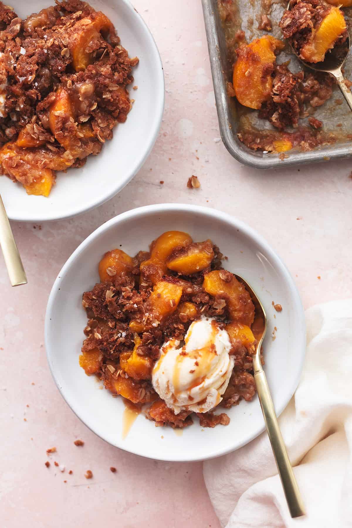 two bowls of peach crisp beside pan of more peach crisp