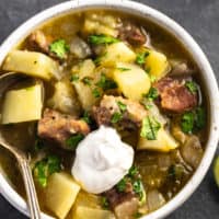 potato and pork stew with green chiles topped with sour cream in a bowl