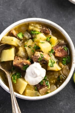 potato and pork stew with green chiles topped with sour cream in a bowl