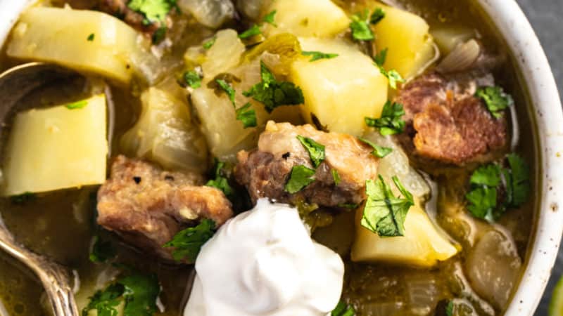 potato and pork stew with green chiles topped with sour cream in a bowl