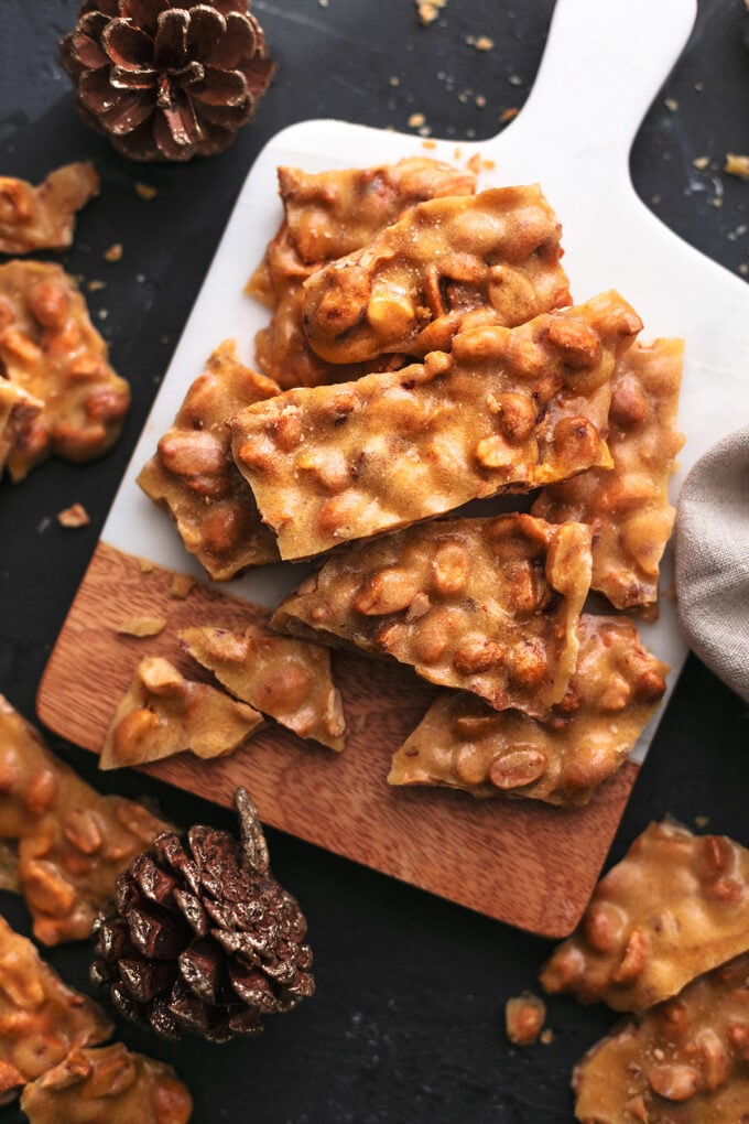 peanut brittle pieces on a cutting board with pinecones and linen
