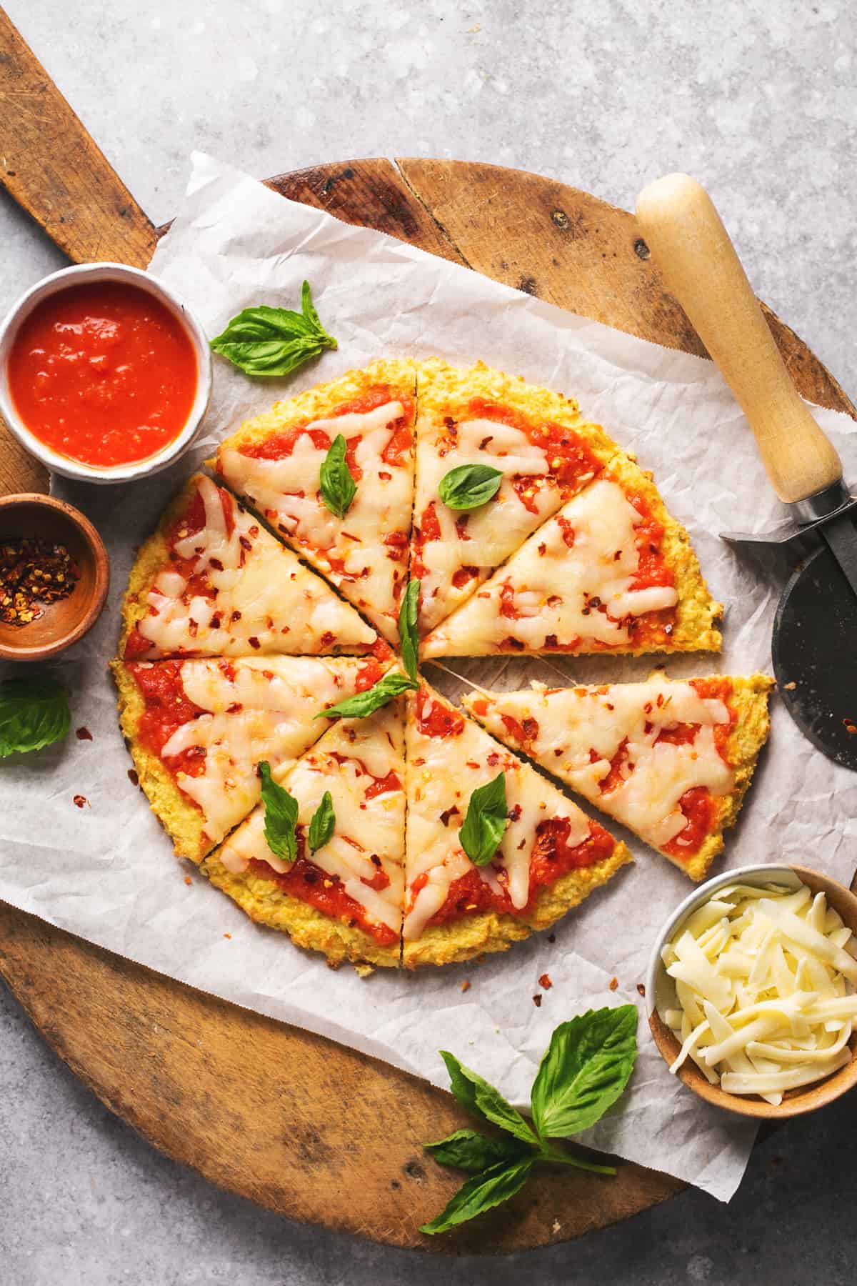 sliced whole pizza on cutting board with toppings and cutter