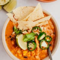 creamy enchilada soup in a bowl with a spoon and toppings
