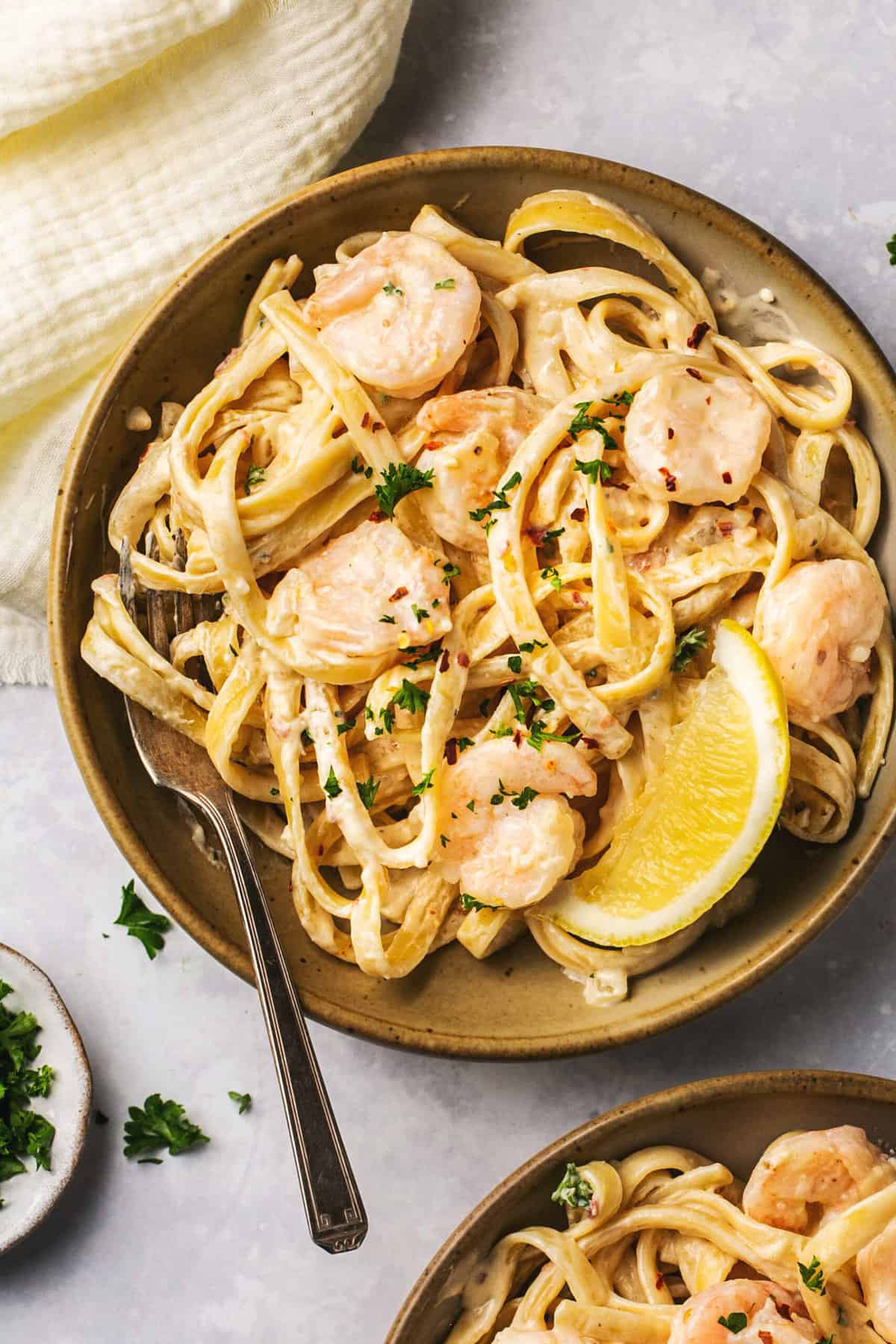 bowl of creamy garlic shrimp pasta with fork and lemon wedge