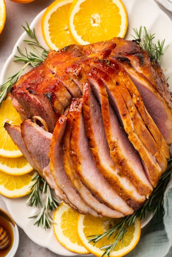 overhead view of sliced honey baked ham on platter with orange slices