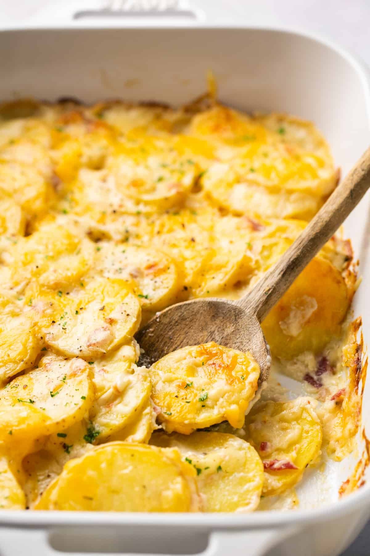 scalloped potatoes in baking dish with wooden serving spoon