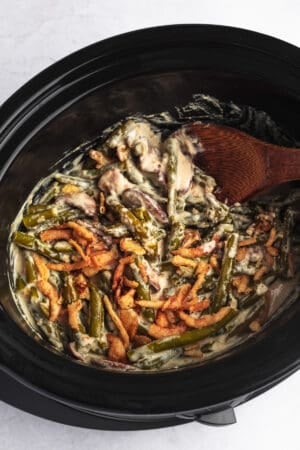 creamy green beans with crispy fried onions and serving spoon in slow cooker