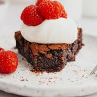 flourless chocolate cake slice topped with whipped cream and raspberries