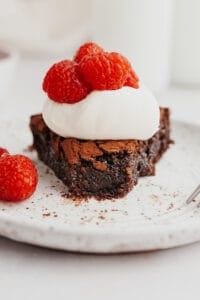 flourless chocolate cake slice topped with whipped cream and raspberries