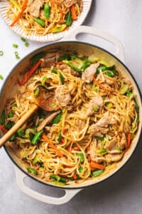 noodles and vegetables in a skillet with a wooden serving spoon