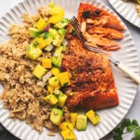 fork cutting into salmon beside mango and rice on a plate