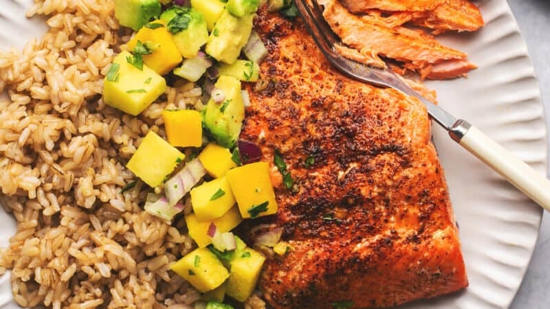 fork cutting into salmon beside mango and rice on a plate