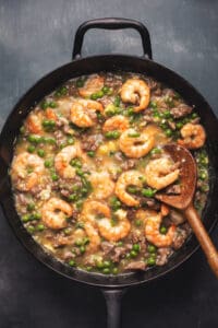 skillet with shrimp and pork and peas in sauce with wooden spoon