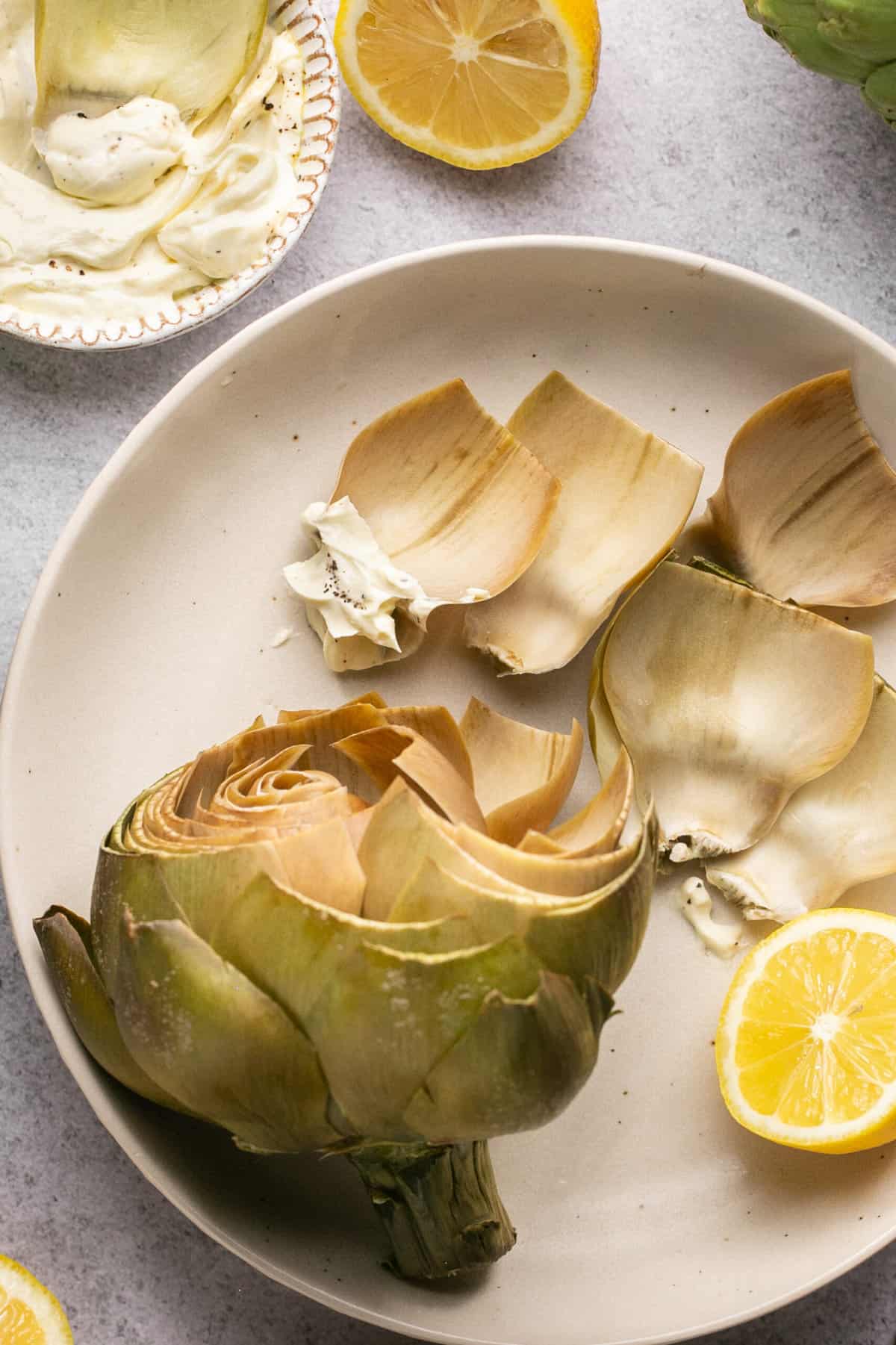 cooked artichoke on a plate with lemon half