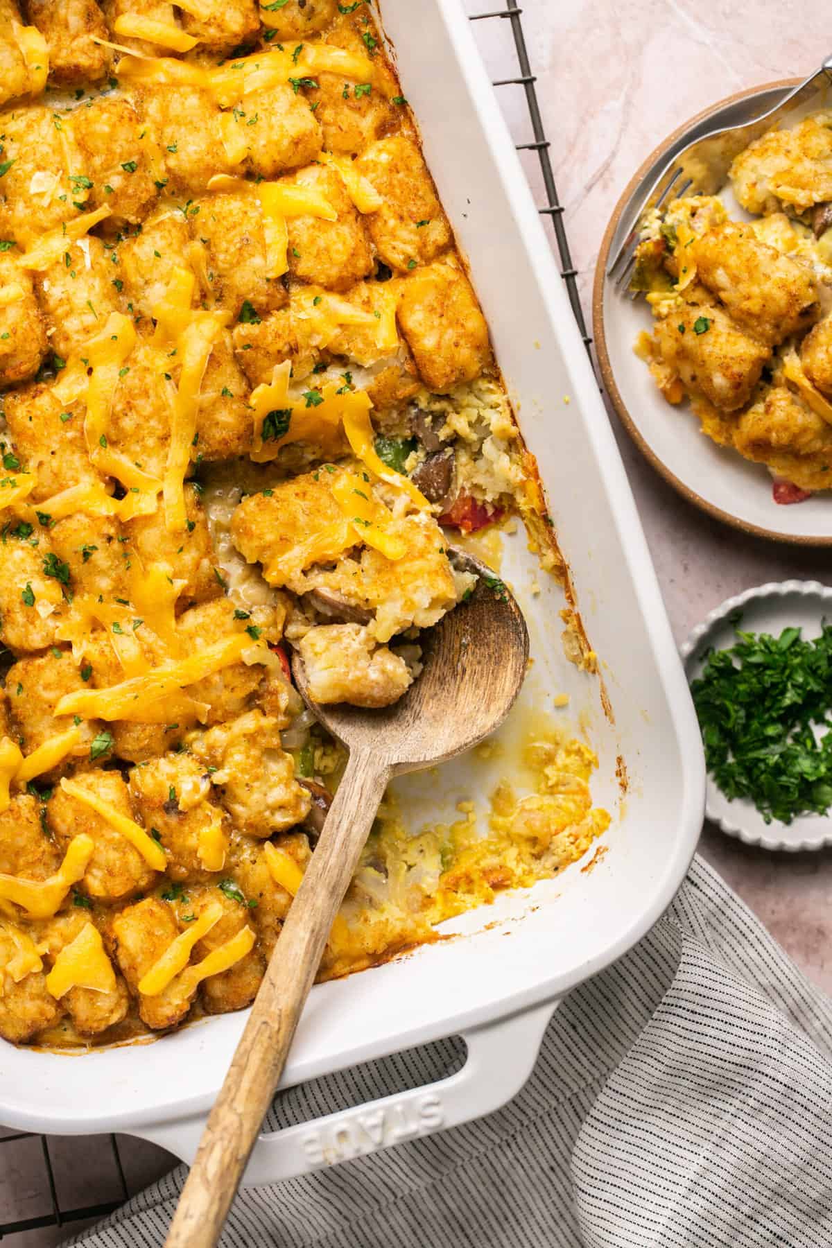 wooden serving spoon scooping tater tots from casserole dish