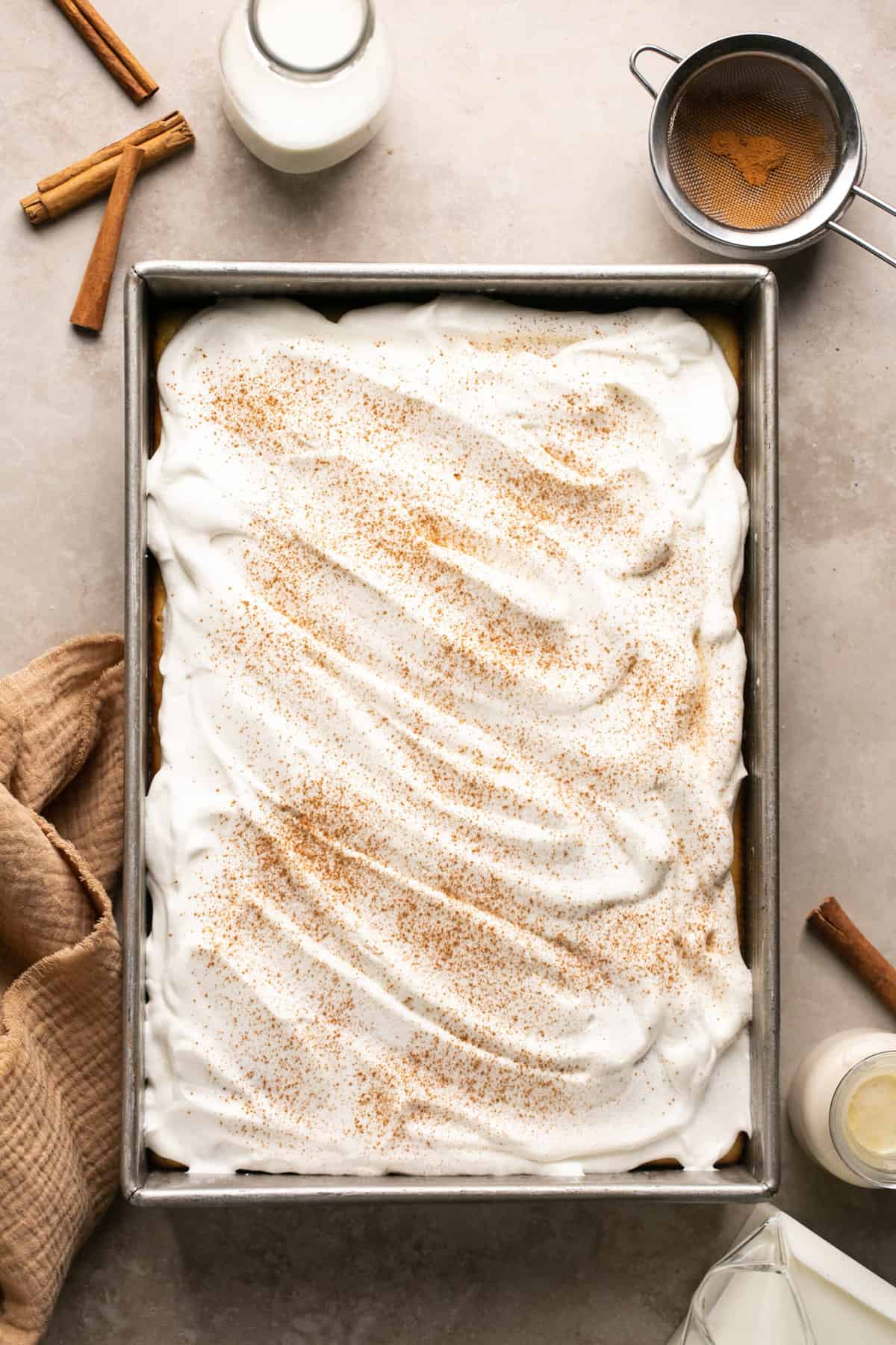 tres leches cake in pan with cinnamon and milk beside