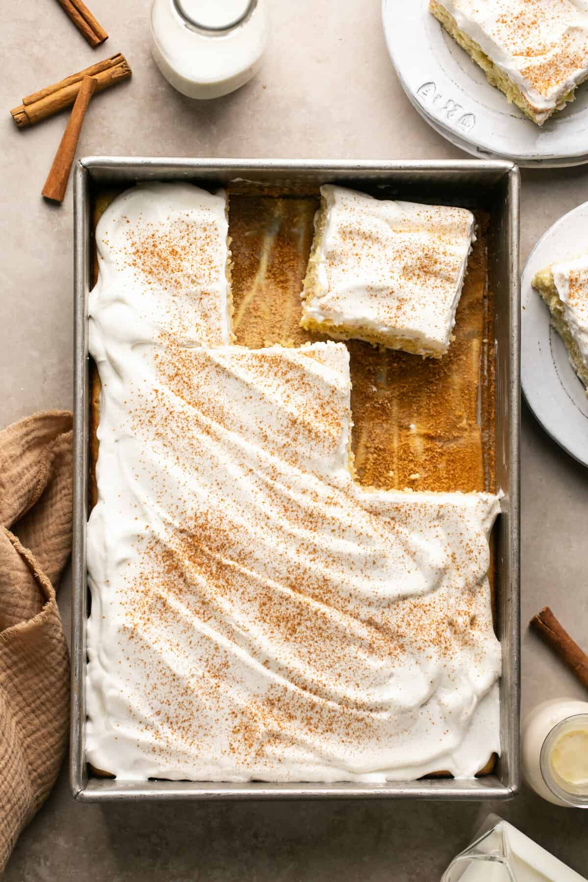 tres leches cake in pan with cinnamon and milk beside