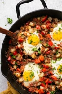 beef and potatoes with veggies and fried eggs on top