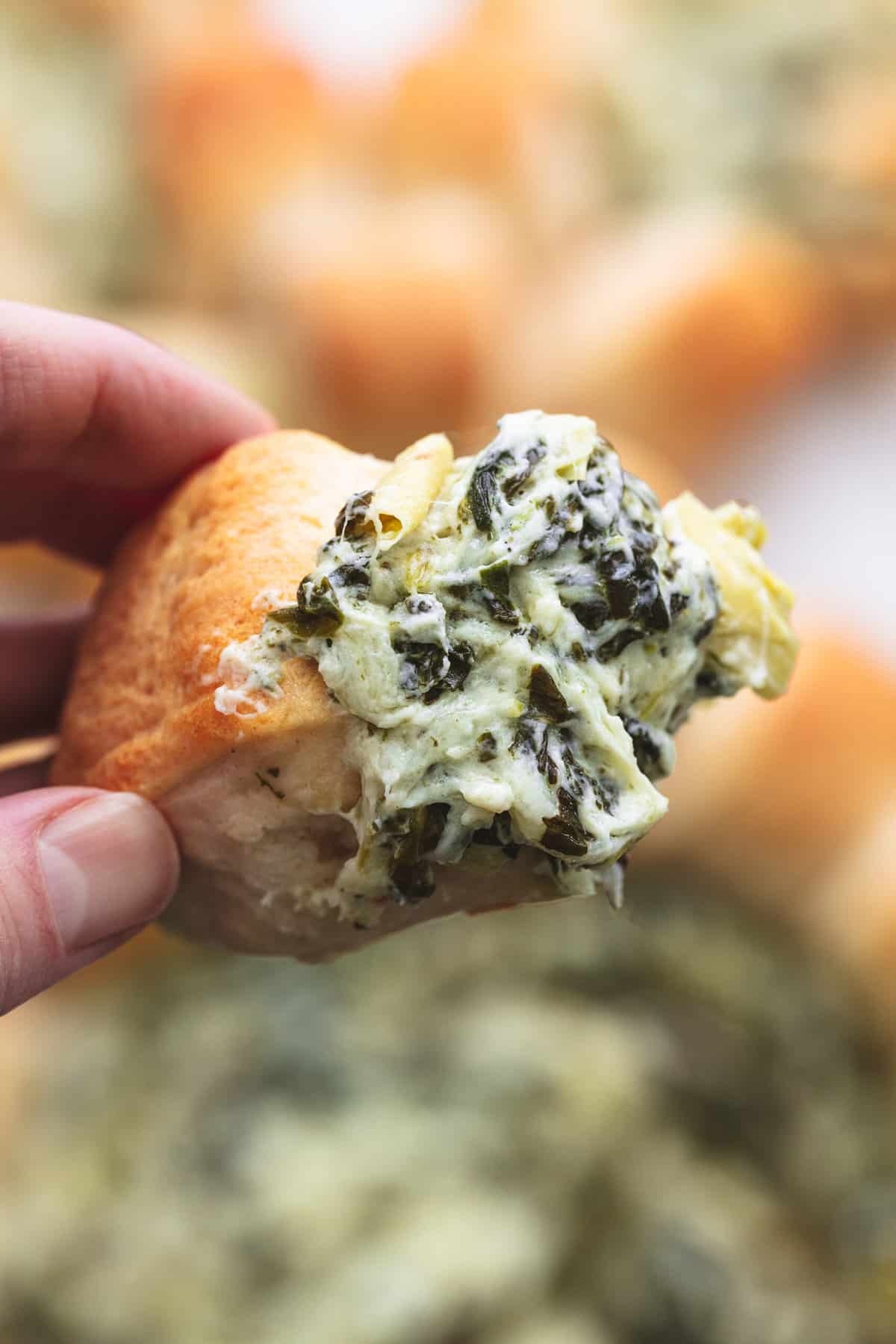 hand holding crescent roll with spinach dip