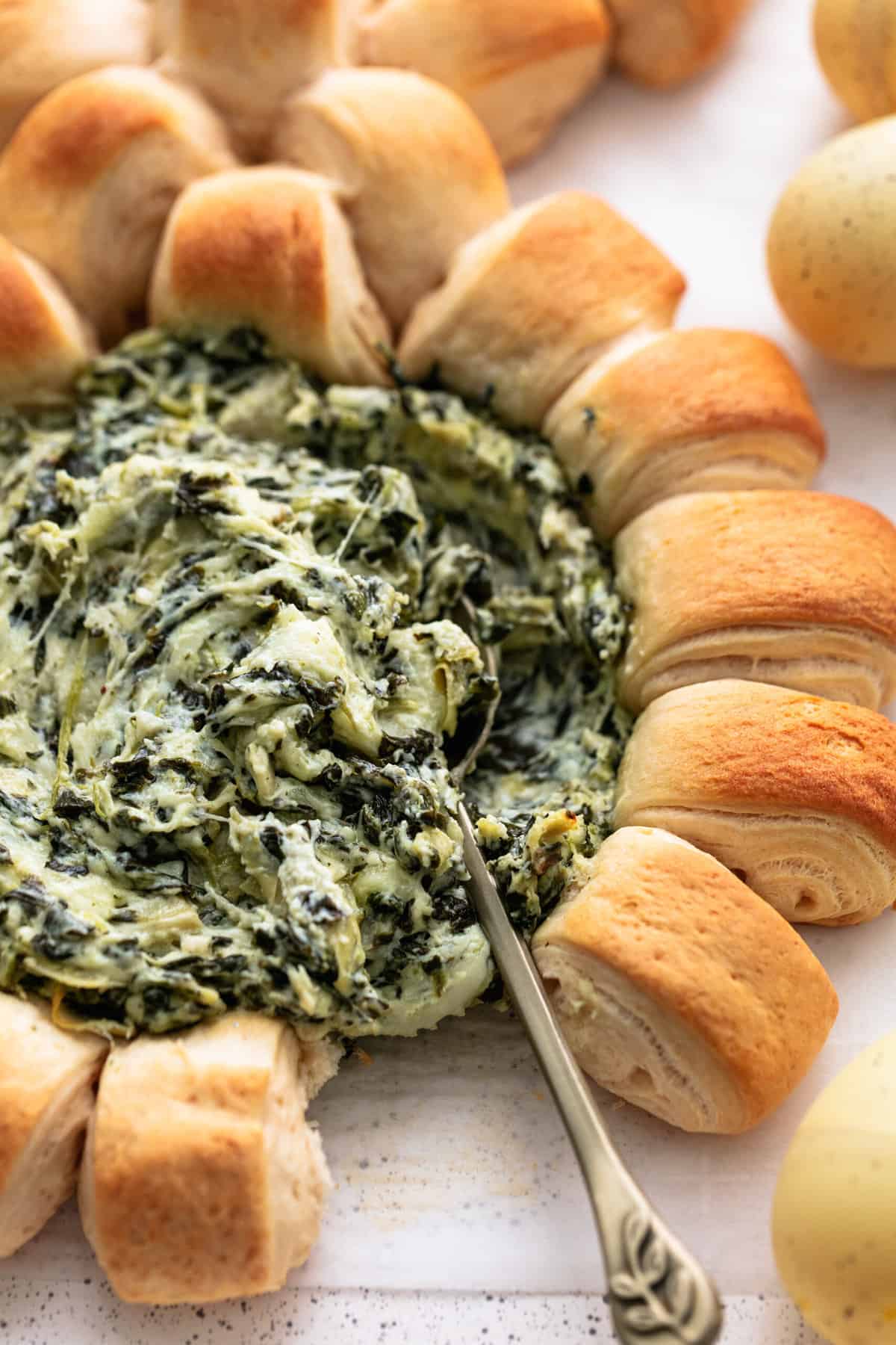 serving spoon dipping into spinach dip with crescent rolls