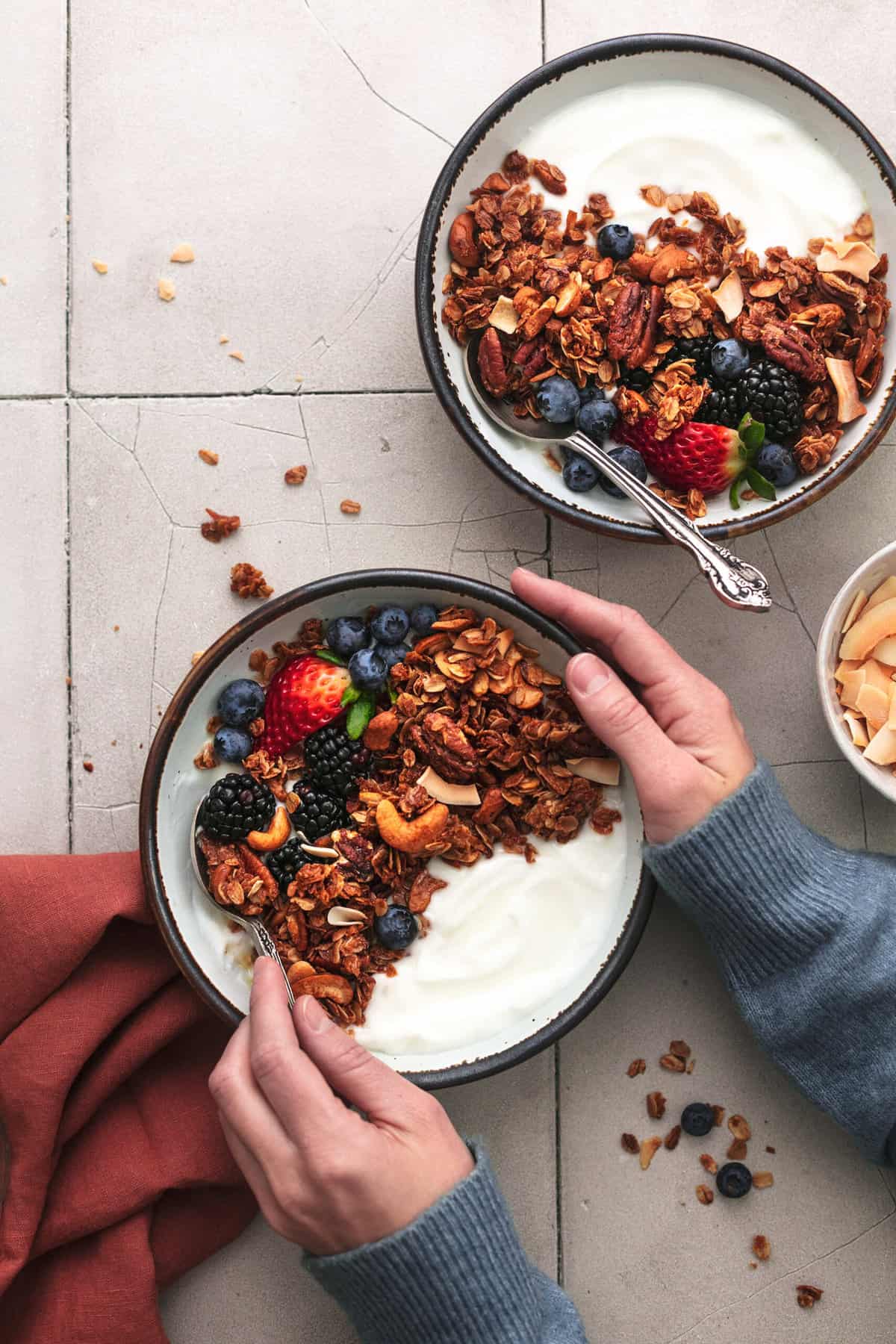 hands holding bowl of yogurt with fruit and nuts