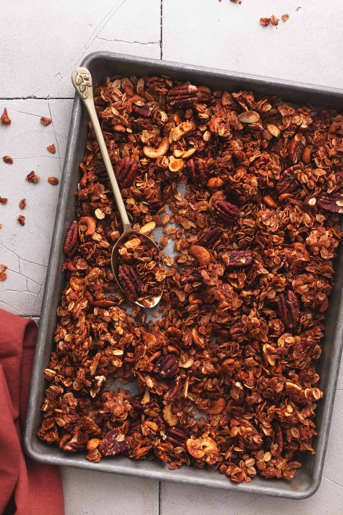 baked granola on a sheet pan with serving spoon