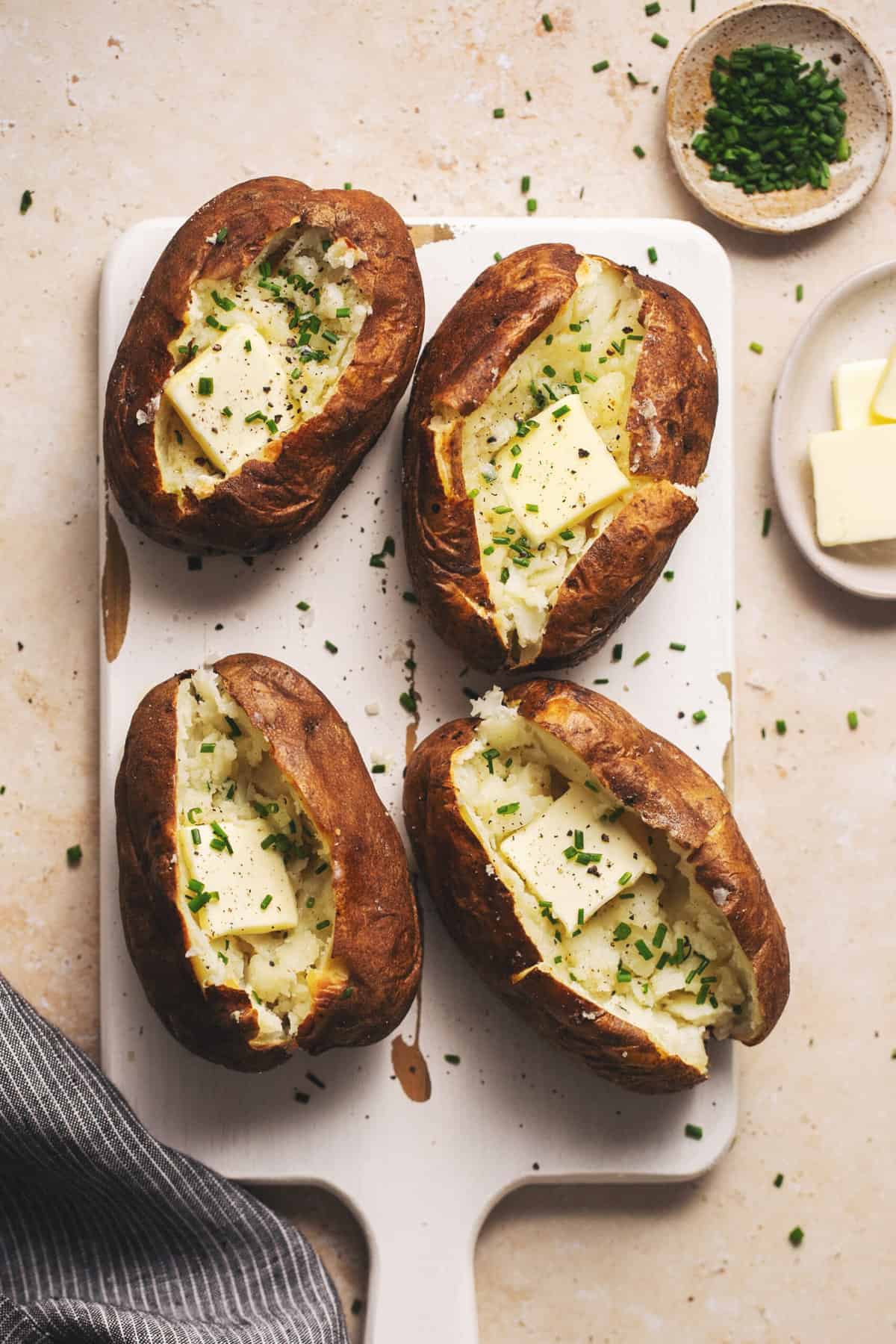 four baked potatoes with butter and chives on serving board