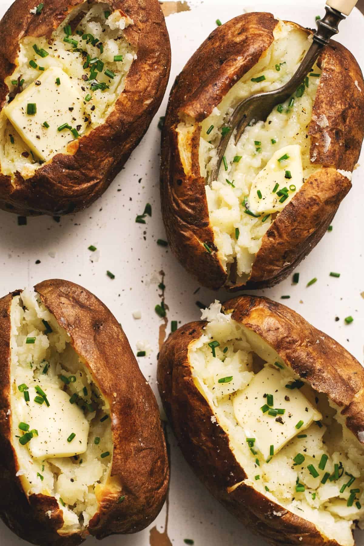 four baked potatoes with butter and chives on serving board