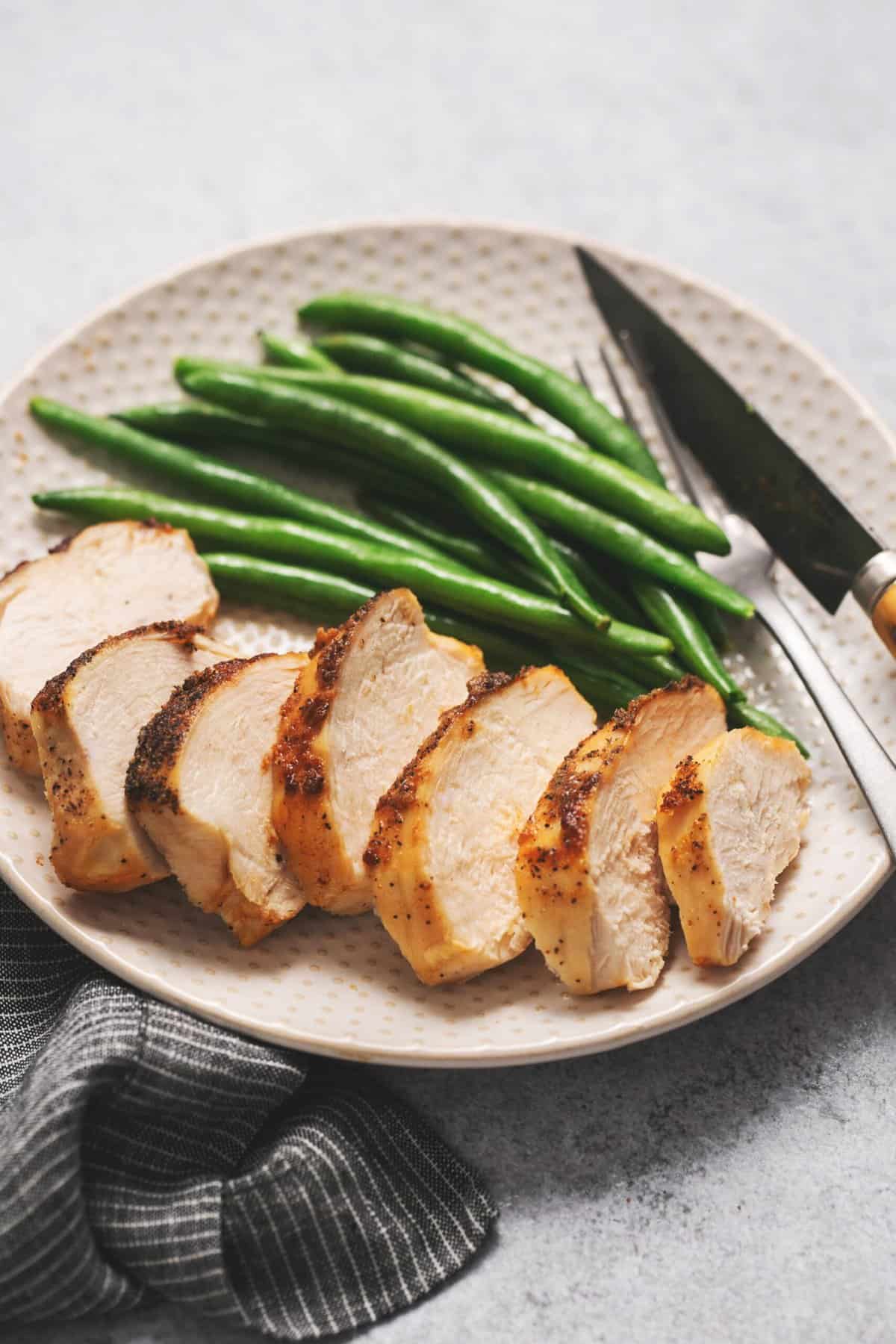 sliced chicken breast on a plate with green beans and knife