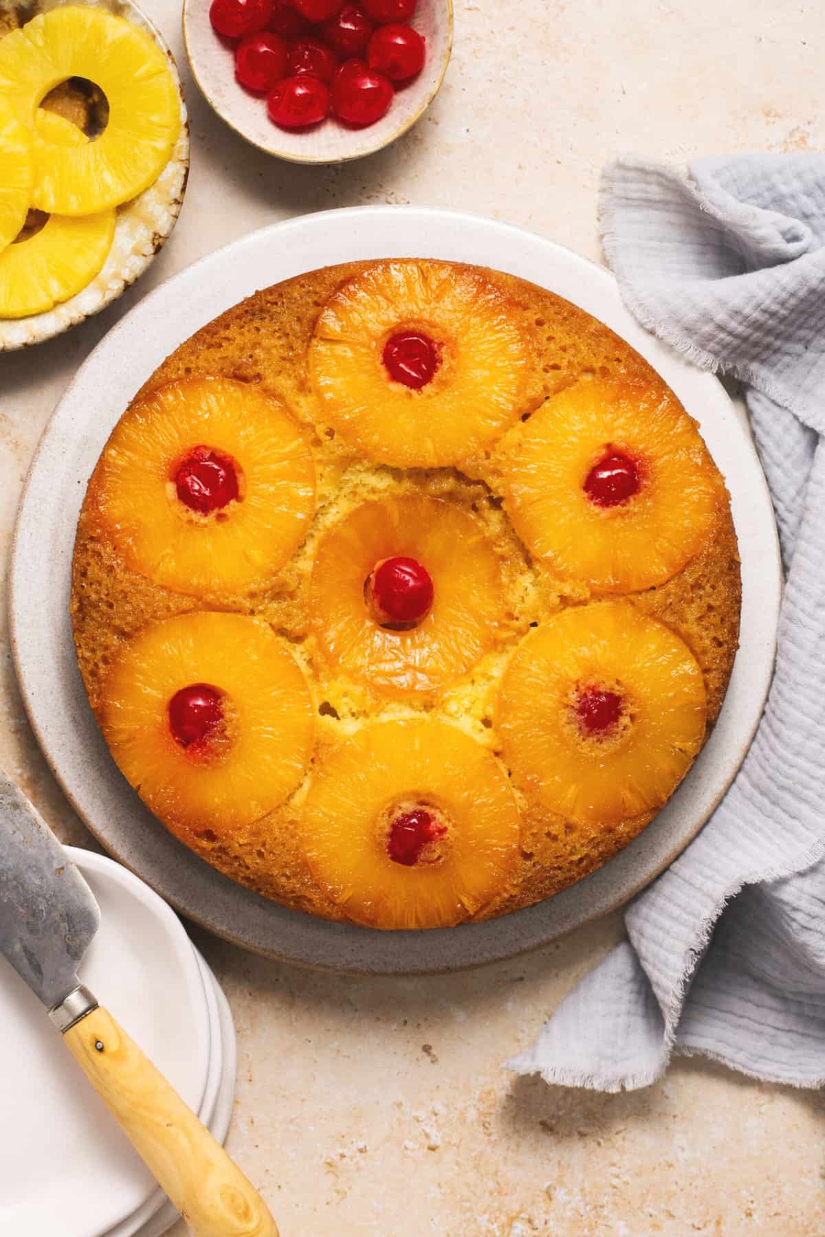 pineapple upside down cake on platter with pineapple rings and cherries on table
