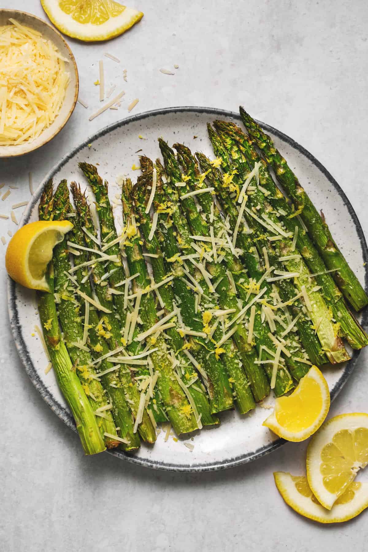 asparagus on a plate with lemon wedges and parmesan