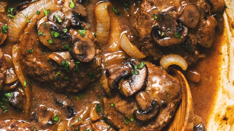 hamburger steaks in skillet with serving spoon