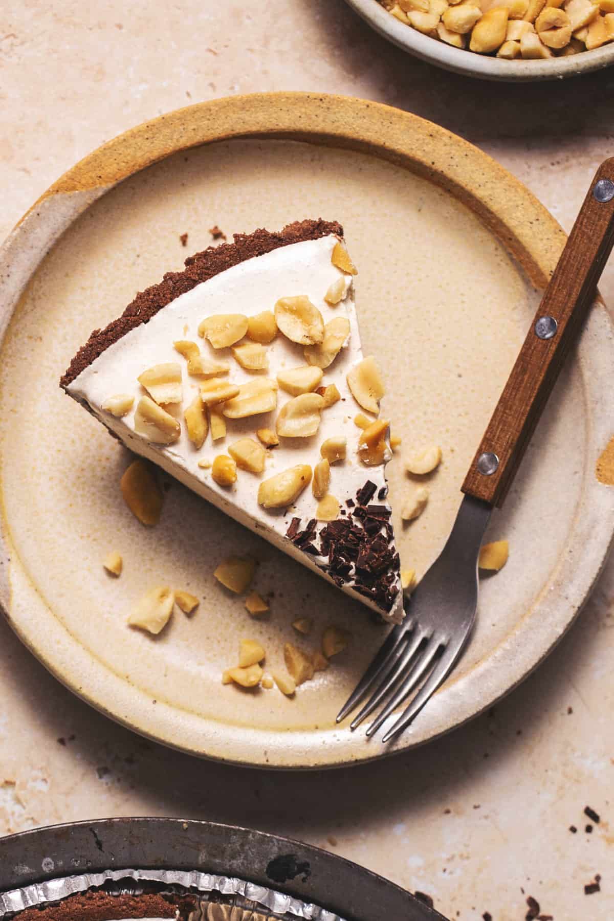 overhead view of peanut butter pie slice with fork on plate with peanuts and chocolate shavings