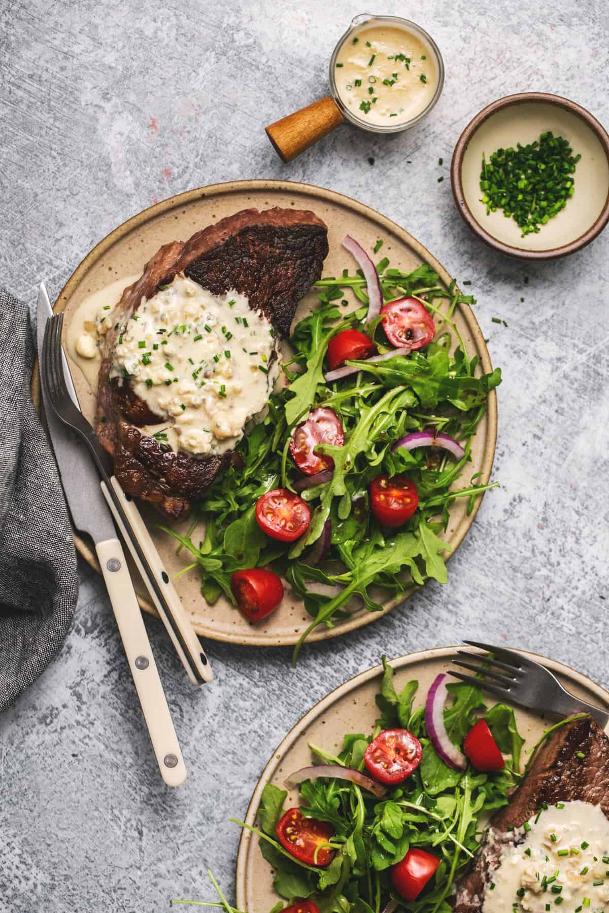 steak and greens on plate with fork and knife and sauce