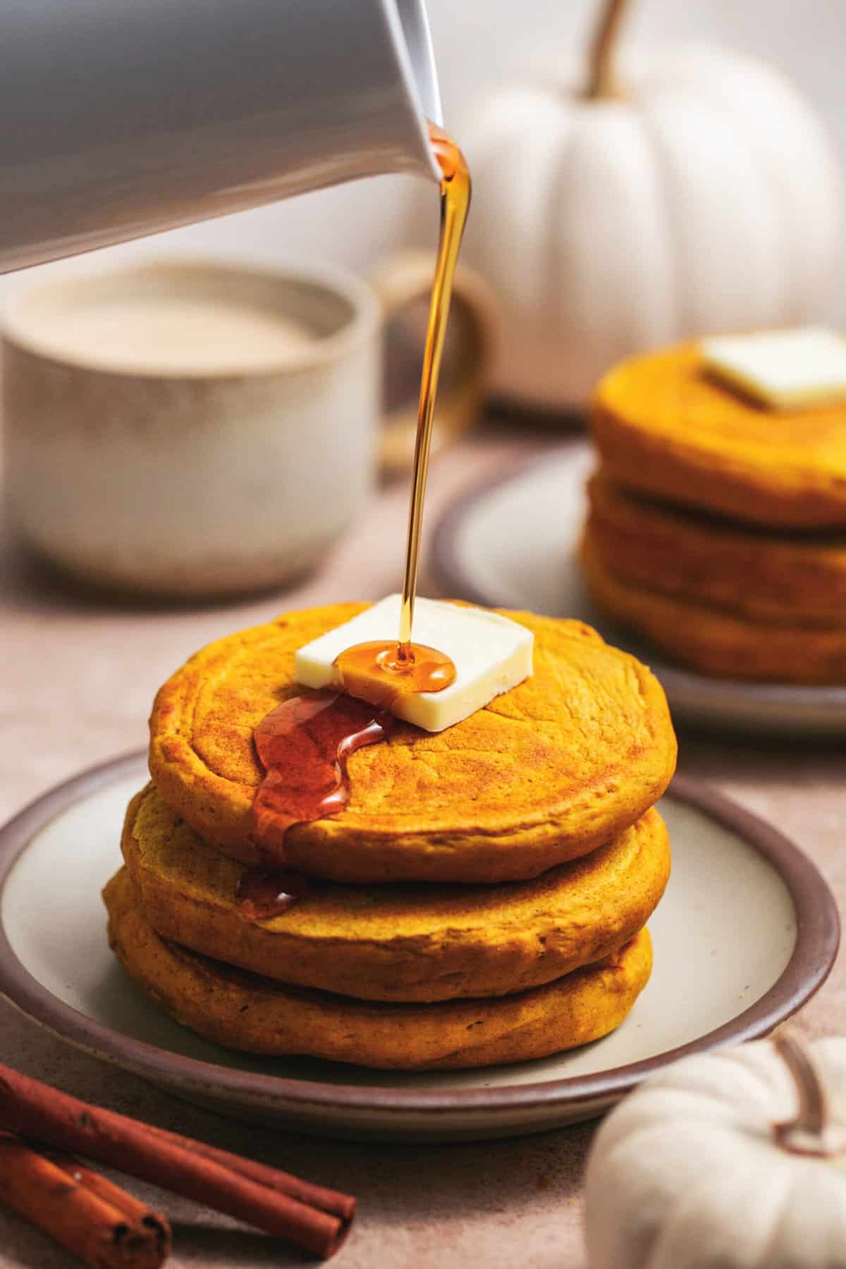 syrup pouring onto stack of pancakes with pat of butter on top