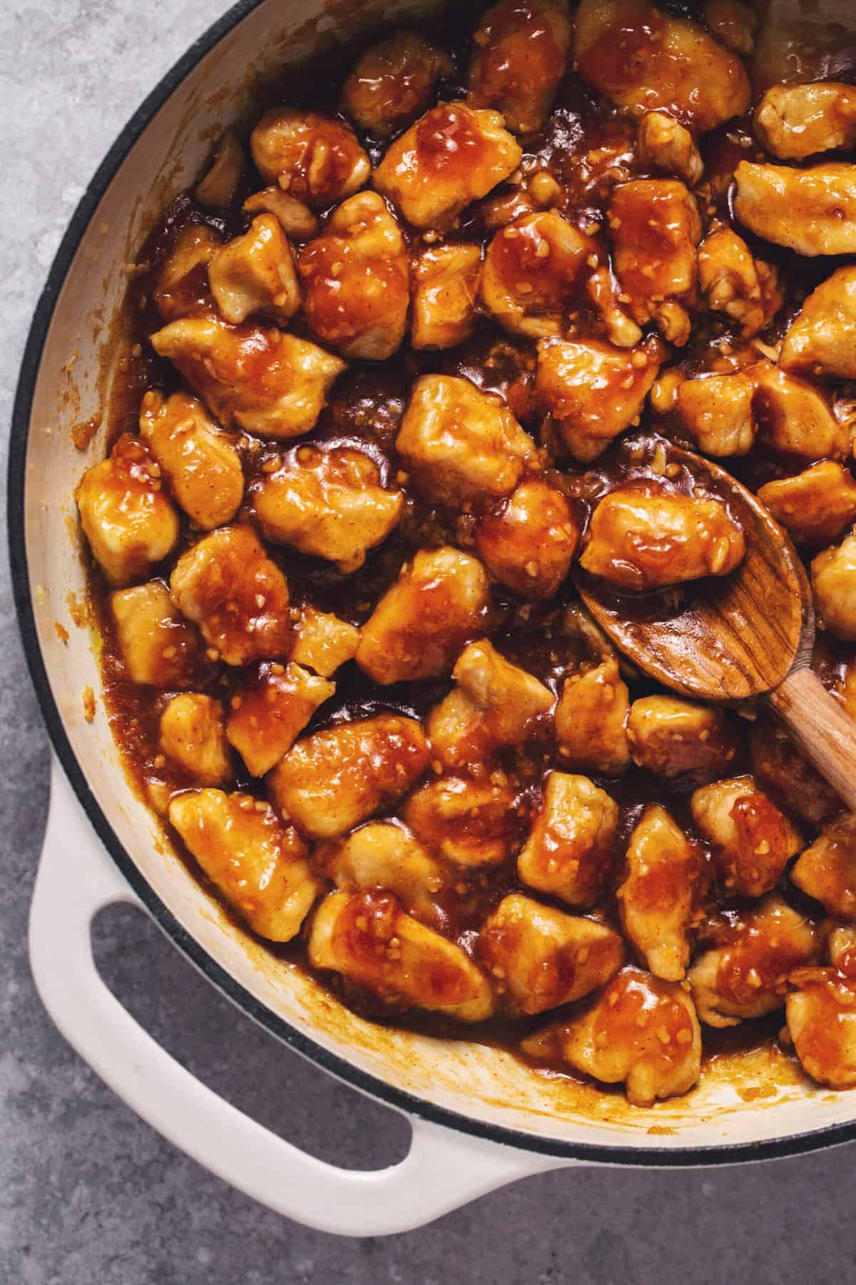 chinese chicken in spicy sauce in skillet with wooden serving spoon