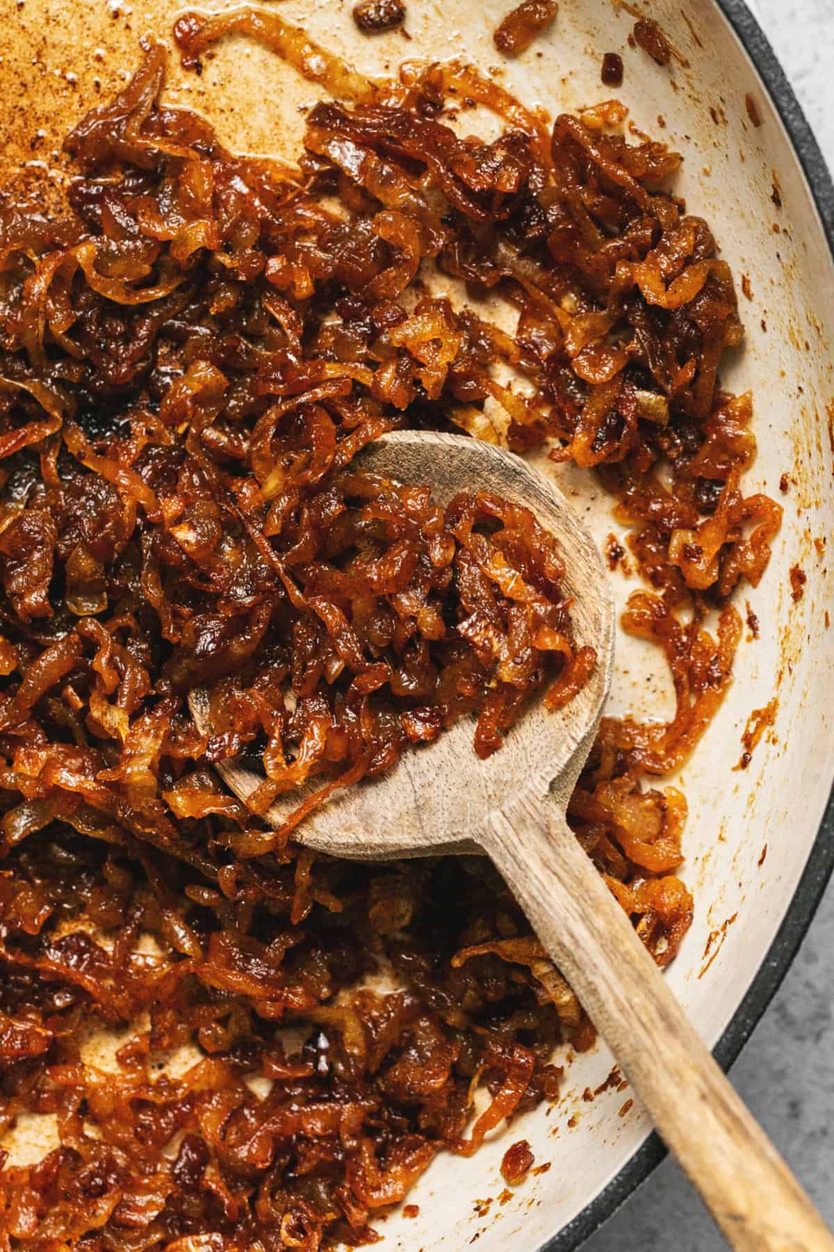 wooden spoon scooping cooked onions from a pan