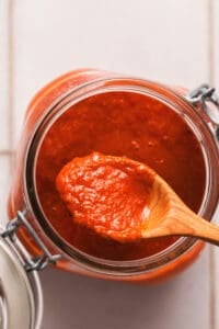 wooden spoon full of enchilada sauce resting on jar of more sauce