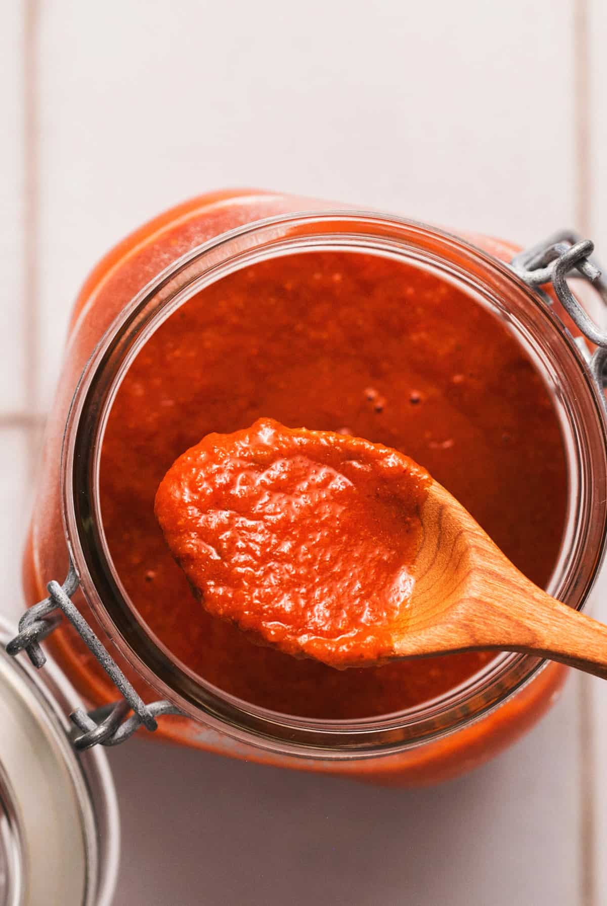 wooden spoon full of enchilada sauce resting on jar of more sauce