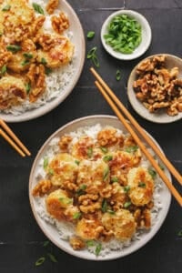 two bowls of honey walnut shrimp with chopsticks and extra toppings in pinch bowls