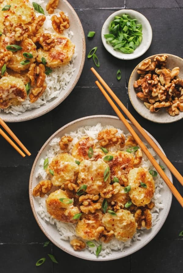 two bowls of honey walnut shrimp with chopsticks and extra toppings in pinch bowls