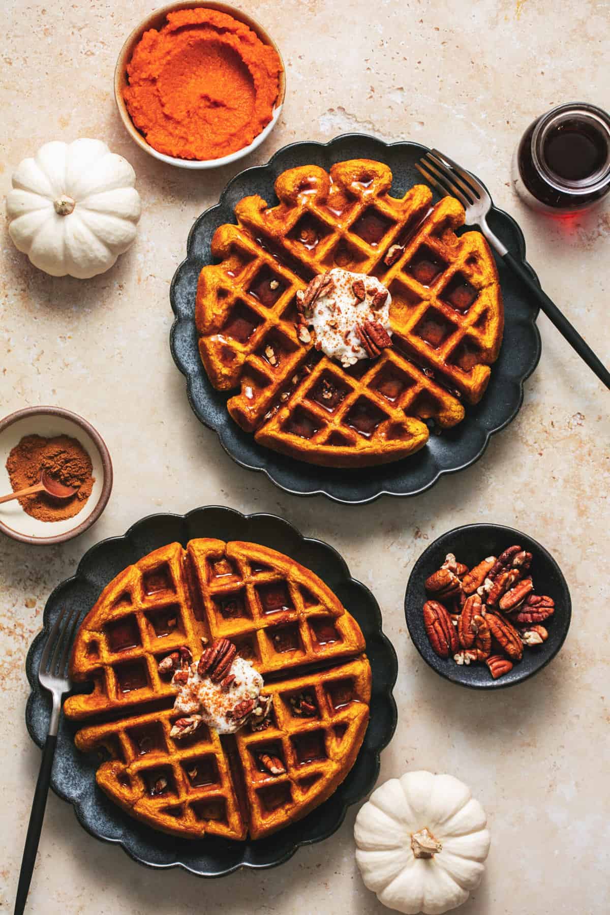 two plates of pumpkin waffles with small white pumpkins and pecans decorating table