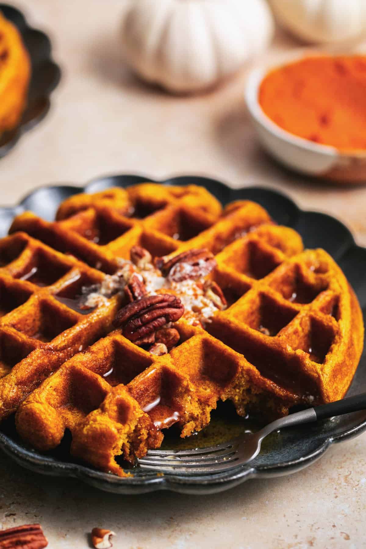 partially eaten waffle on plate, topped with whipped cream and pecans