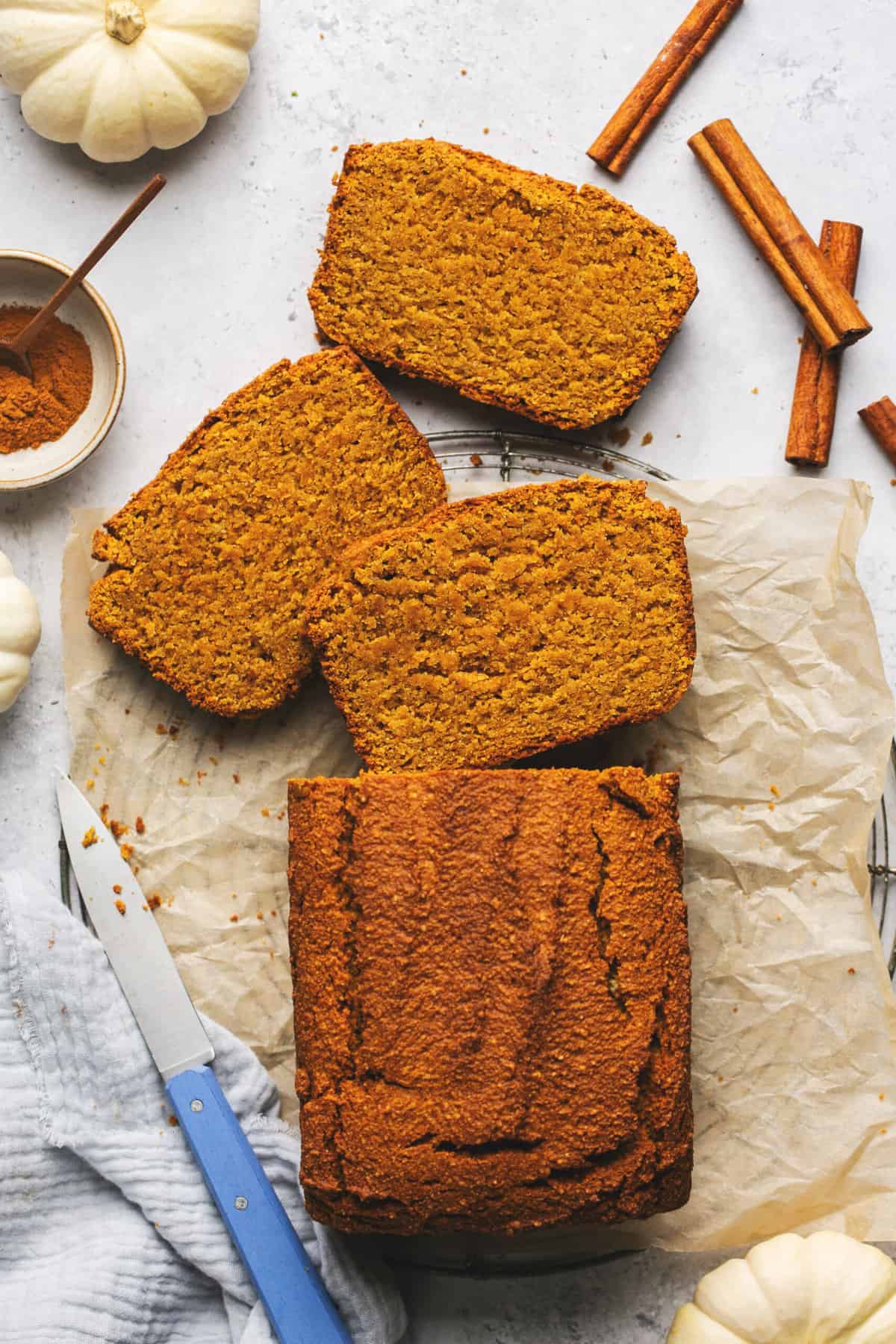 partially sliced pumpkin bread with bread knife and cinnamon sticks on table