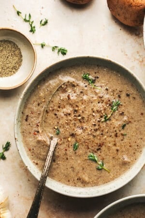 bowl of mushroom soup topped with black pepper and thyme and spoon in bowl