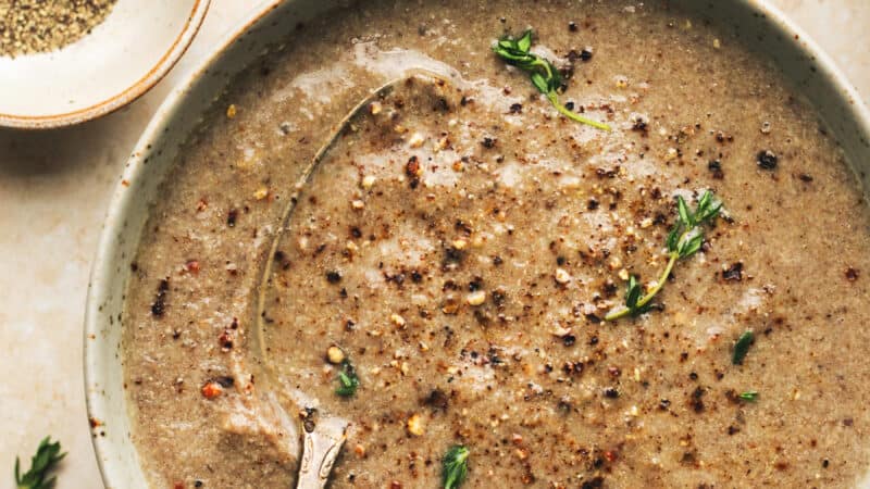 bowl of mushroom soup topped with black pepper and thyme and spoon in bowl