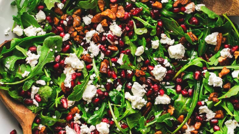 salad in bowl with greens, nuts, pomegranate, and crumbled cheese