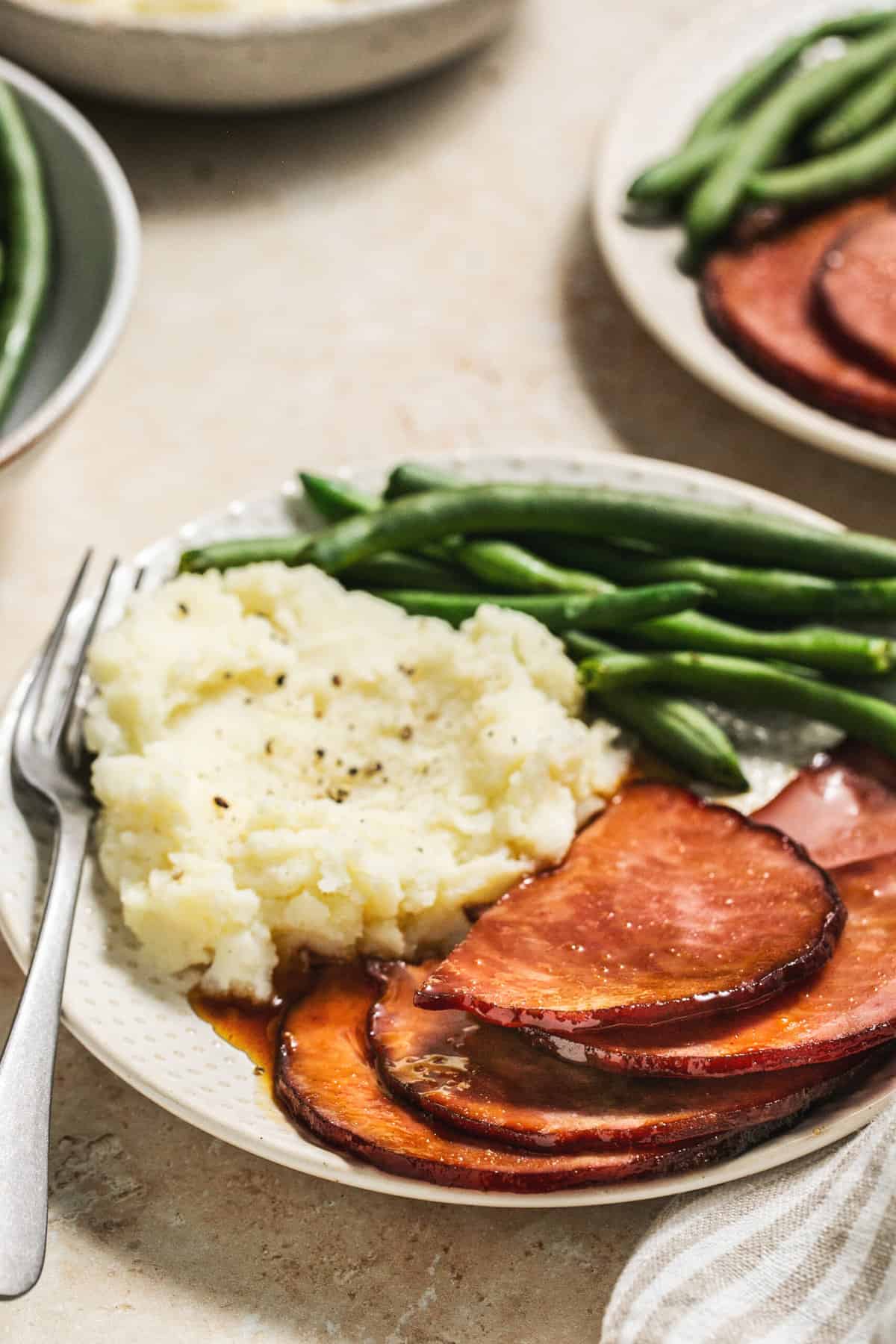 plate of sliced ham, mashed potatoes, and green beans