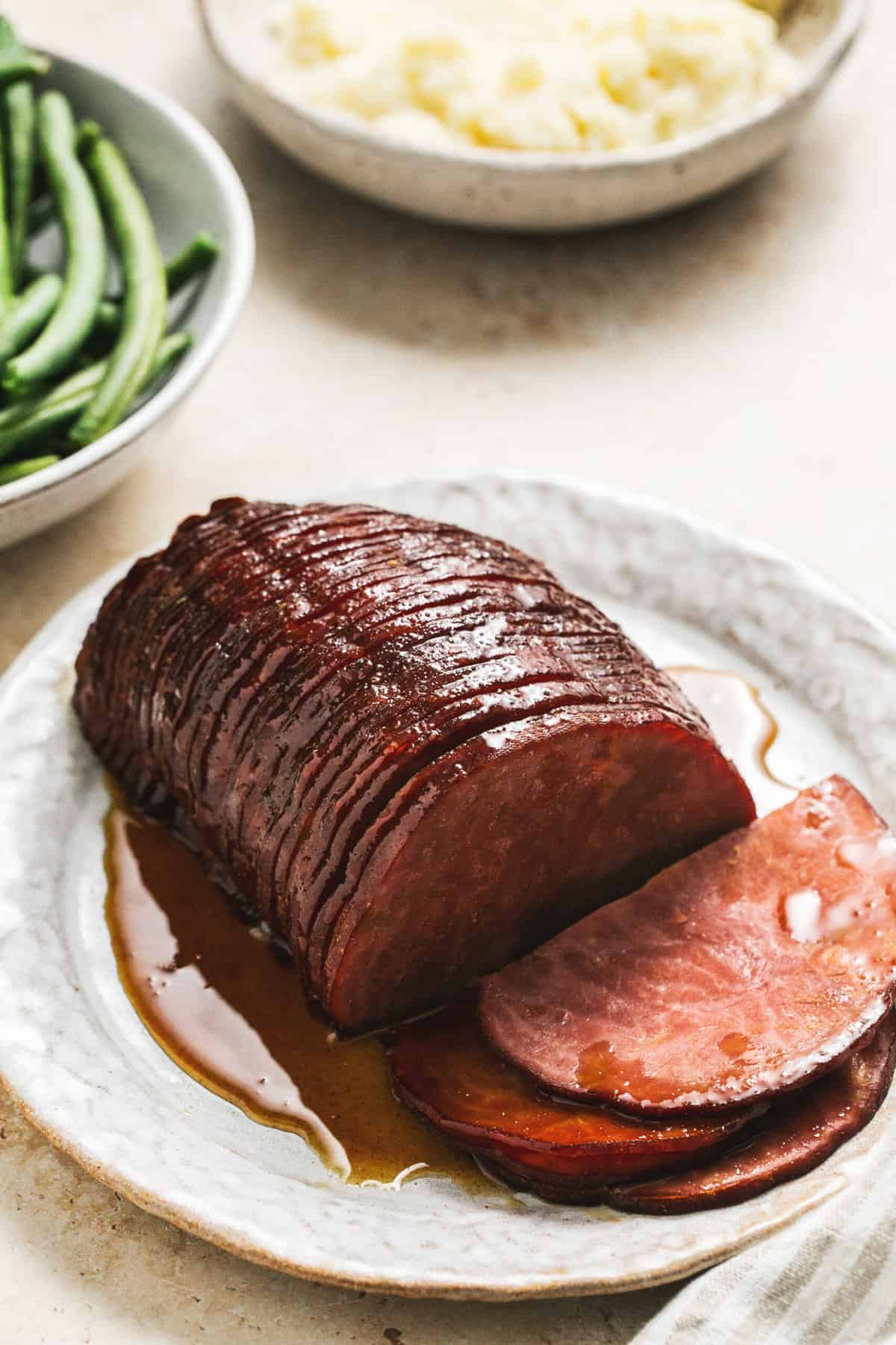 platter of glazed ham with green beans and potatoes in background