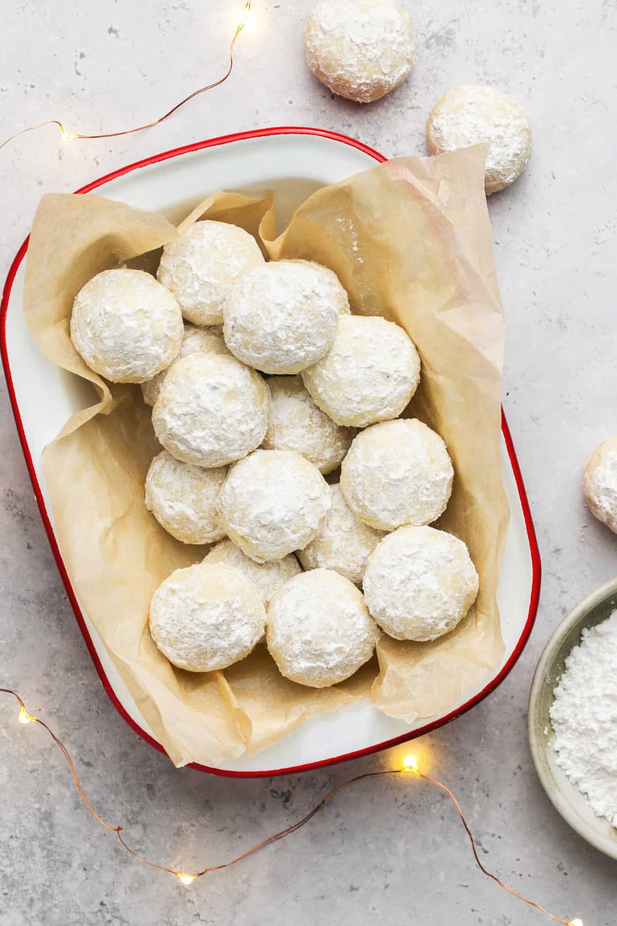 christmas snowball cookies in serving dish with twinkle lights and ingredient bowls